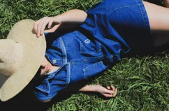 Vestido corto de jean color gris oscuro con efecto acid wash, sin mangas, con cuello camisero y cierre frontal de botones. Incluye dos bolsillos en el pecho con solapa y pespuntes decorativos.