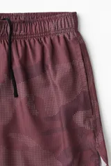 Short deportivo de doble capa, con calza interior. El short exterior es de color borgoña con un estampado sutil de puntos en forma de camuflaje. Posee cintura elástica con cordón oculto y aberturas laterales. La calza interior es negra.