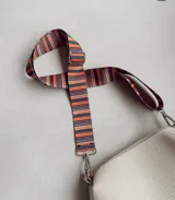 Correa intercambiable y ajustable para cartera, confeccionada en cinta tejida con diseño de rayas multicolores y herrajes metálicos plateados con ganchos tipo mosquetón.