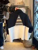 Buzo combinado con parte superior negra, parte inferior de corderito blanco y un inserto triangular con diseño geométrico tejido en tonos marrones y blancos en la espalda.