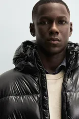 Campera puffer negra con capucha, cierre frontal con cremallera, bolsillos laterales con cremallera y puños elásticos.