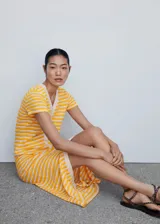 Vestido midi de punto con diseño de rayas horizontales amarillas y blancas. Presenta cuello en pico, manga corta y cierre frontal completo con botones. Su diseño es de corte recto.