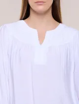 Blusa blanca de rayón y poliéster con textura, escote en V y delicados bordados al tono sobre el canesú. Cuenta con mangas raglán tres cuartos abullonadas con puños elastizados y diseño holgado.