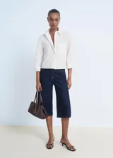 Camisa de corte recto y diseño crop, confeccionada en popelín de algodón. Presenta cuello camisero, cierre frontal con botones, mangas tres cuartos y un bolsillo en el pecho con detalle de strass.