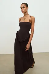 Vestido largo de color negro con escote recto y tirantes finos ajustables. Presenta un diseño con detalle de volante tipo peplum en la cintura y falda con caída fluida.