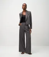 Pantalón de vestir gris oscuro, modelo wide leg, con cintura traspasada y hebilla metálica. Presenta pliegues delanteros marcados y bolsillos traseros.