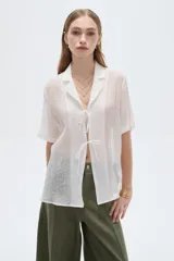 Blusa blanca de lyocell con cuello solapa, mangas cortas y cierre frontal mediante cordones para anudar.