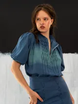 Blusa azul de algodón tipo seda, teñida a mano con técnica tie dye. Tiene corte recto, mangas cortas abullonadas con elástico y cierre invisible en el escote delantero.
