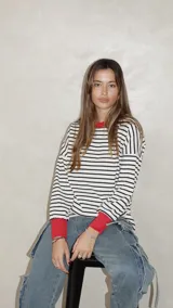 Sweater de punto con diseño a rayas horizontales en blanco y negro, cuello redondo y puños en color rojo vibrante. Presenta un calce relajado y holgado.