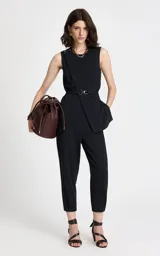 Chaleco sastrero de corte entallado con diseño de raya diplomática vertical. Presenta cuello redondo, sisas sin mangas, detalle cruzado asimétrico en el frente, botones decorativos en el hombro izquierdo y cinturón de tela a juego con hebilla metálica.