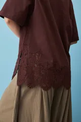 Remera blanca de algodón, de corte oversize, manga corta y cuello redondo, con detalle de aplique de encaje floral en el borde inferior.
