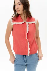 Chaleco de tejido de punto color coral/terracota, sin mangas, con cuello polo y ribetes de volados en color beige contrastante en el cuello y el frente.