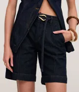 Bermuda de tiro medio confeccionada en denim de algodón color azul oscuro, con bolsillos laterales y pespuntes en contraste. Incluye un cinturón de tela con hebilla metálica de diseño original.