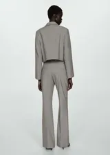 Chaqueta corta de diseño recto y estilo sastrero, confeccionada en tejido fluido color gris. Presenta cuello camisero, cierre frontal con botones ocultos y dos bolsillos de parche en el frente.