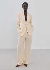 Blazer de diseño recto y estilo sastrero, color beige, confeccionado en mezcla de lyocell y poliéster. Cuenta con cuello en pico con solapas de muesca, manga larga, bolsillos delanteros con solapa y cierre frontal de un botón.