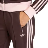 Pantalón deportivo Adidas de corte recto y estilo clásico, color marrón con franjas laterales en tono rosado. Cuenta con cintura elástica con cordón ajustable, bolsillos laterales con cierre y el logo del trifolio bordado en una de las piernas.