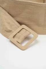 Cinturón ancho de tela color beige, con hebilla cuadrada forrada en el mismo material.