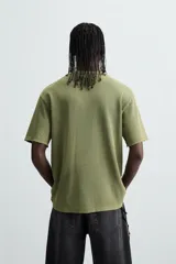 Camiseta de punto de algodón con corte relaxed fit, cuello redondo y manga corta. Color verde oliva con efecto lavado y estampado frontal con diseño gráfico en tonos rojo y amarillo.
