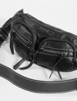 Riñonera de cuero sintético color marrón con acabado suave. Presenta un compartimento principal con cierre y dos bolsillos frontales adicionales con cierres metálicos y tiradores de cuero. Incluye logo metálico de la marca en el frente.