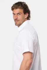 Camisa lisa de manga corta color crema, confeccionada en 100% algodón, con cuello abotonado y un bolsillo en el pecho.