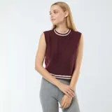 Chaleco de tejido de punto color bordó, sin mangas, con cuello redondo y puños acanalados con doble franja blanca. Presenta un patrón de trenzas verticales.