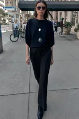 Pantalón de vestir marrón oscuro, tiro alto, con pernera ancha y pinzas frontales. Presenta un bolsillo con tapeta en la parte superior delantera.