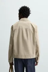 Cazadora color beige de algodón, corte recto, con cuello solapa, cierre frontal con cremallera, manga larga con puños abotonados y bolsillos laterales de ojal.
