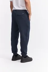 Pantalón de jogging color gris melange, confeccionado en tejido de algodón y poliéster. Presenta cintura elástica con cordón de ajuste, bolsillos laterales con cierre y puños elásticos en los tobillos.