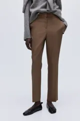 Pantalón tobillero color marrón, de tejido elástico, con cintura estándar y elástico oculto. Presenta cierre con corchete oculto, bolsillos al bies y bolsillos traseros decorativos. Las piernas son ajustadas.