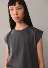 Camiseta blanca de algodón con cuello redondo y mangas cortas con tachas decorativas en los hombros.