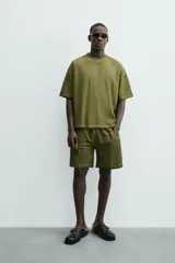 Camiseta de algodón de corte relajado (relaxed fit) con cuello redondo y manga corta. Presenta un tejido acanalado vertical (canalé) y un acabado ligeramente desgastado o lavado en tono verde oliva.