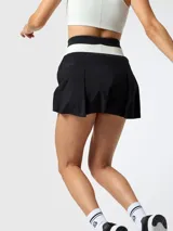 Falda pantalón deportiva de color negro con pretina ancha tejida en franjas blanca y negra, diseño plisado al frente y shorts internos.
