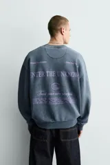 Sudadera de corte boxy fit con efecto lavado, cuello redondo y manga larga. Presenta estampados a contraste en color violeta en la parte frontal y acabados en rib en cuello, puños y ruedo.