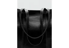 Bolso tipo tote color negro de acabado brillante y textura arrugada, con asas largas de hombro y costuras verticales decorativas en el frente.
