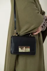 Cartera negra de cuero sintético con broche metálico dorado y asa corta. Incluye correa larga desmontable para usar como bandolera.