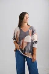 Sweter de punto con diseño geométrico abstracto en tonos grises, marrones y beige. Presenta escote en V, corte holgado y mangas largas con puños vueltos.