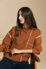 Sweater de punto color marrón con diseño de líneas blancas en contraste. Presenta cuello redondo, mangas largas y puños tejidos, con una estética minimalista y moderna.