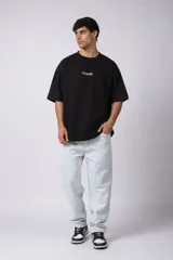 Remera de corte oversize color negro, con cuello redondo y estampa frontal pequeña con la palabra 'REWIND' en color blanco.