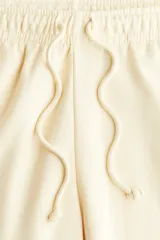 Jogging de felpa color amarillo pálido, con interior cepillado suave. Presenta cintura elástica fruncida con cordón ajustable y elástico revestido en los bajos.