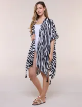 Kimono confeccionado en gasa ligera de poliéster, con diseño estampado animal print de cebra en color blanco y negro. Presenta silueta amplia, mangas cortas integradas y ruedo asimétrico con detalles de borlas en las puntas.