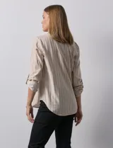 Blusa de manga larga con escote en V, confeccionada en tejido ligero con estampado de rayas verticales en tonos beige y blanco. Presenta un diseño con pliegue frontal y mangas ajustables mediante presilla y botón.