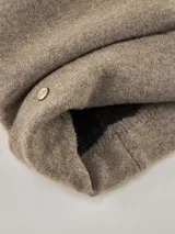 Gorro tipo beanie de lana color gris con vuelta y detalle de chapa metálica circular con logo de la marca en el frente.