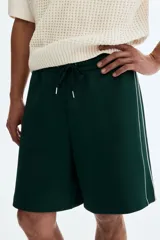 Short de corte relajado de color verde oscuro, con cintura elástica y cordón ajustable. Cuenta con ribetes de cinta blanca a lo largo de los laterales y bolsillos frontales.