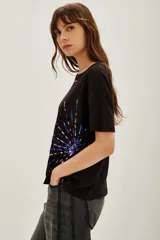 Remera negra de manga corta con cuello redondo, decorada con apliques de lentejuelas azules y doradas dispuestas en forma de explosión o rayos.