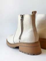 Bota corta de cuero vacuno con textura granulada, color crudo. Presenta cierre lateral metálico, suela track de goma en tono suela y tirador trasero.