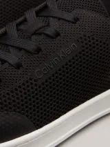 Zapatillas de perfil bajo Calvin Klein, confeccionadas en tejido de punto transpirable color negro. Presentan puntera revestida, trabilla trasera de piel y suela de goma blanca con logo grabado en la mediasuela.