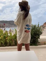 Camisa oversize de lino a rayas blancas y rosadas, con mangas largas y diseño bordado de peces en la espalda.