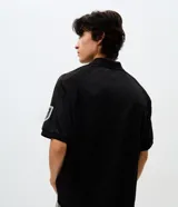 Polo de manga corta con cuello camisero y cierre frontal de botones. Presenta un diseño boxy fit con estampado gráfico en el pecho y detalle en la manga. Confeccionada en tejido técnico de microfibra.