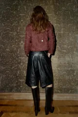 Bermuda negra de tiro alto con efecto piel, bolsillos delanteros y falsos bolsillos de vivo en la espalda. Cierre frontal con cremallera, botón interior y gancho.