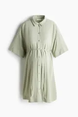 Vestido camisero corto de viscosa color verde menta, con cuello camisero, cierre frontal con botones, hombros caídos y mangas cortas. Incluye un cordón fino para atar debajo del busto.